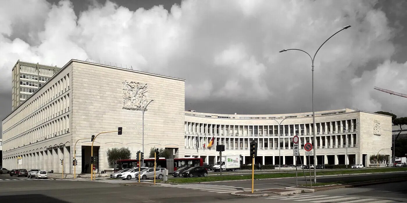 资料图：罗马EUR区的INPS大楼，白色石材外墙、正面刻有ISTITUTO NAZIONALE DELLA PREVIDENZA SOCIALE字样，门前路口有车辆和红绿灯（图：Blackcat / CC BY-SA 4.0，摄于2018年3月13日，资料图）