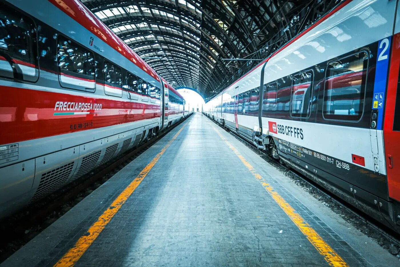 示意图:米兰中央车站站台旁的高铁列车,左侧为 Trenitalia 红灰涂装的 Frecciarossa 1000,右侧为一列印有 SBB CFF FFS 标识的列车,站台边缘画有黄色安全线(图:Cristian Manieri / Pexels,图库资料图)